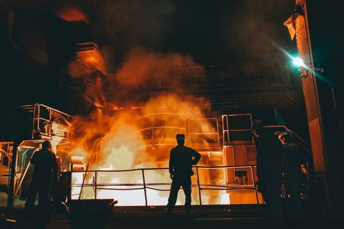 American Steel Mill Interior Workers in hard hats on the floor of a domestic steel mill, surrounded by coils of rolled steel