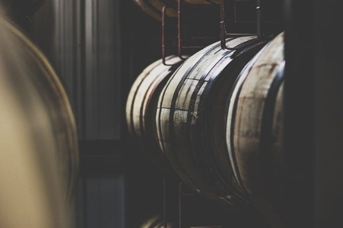 Rows of charred oak bourbon barrels stacked inside a Kentucky distillery warehouse.