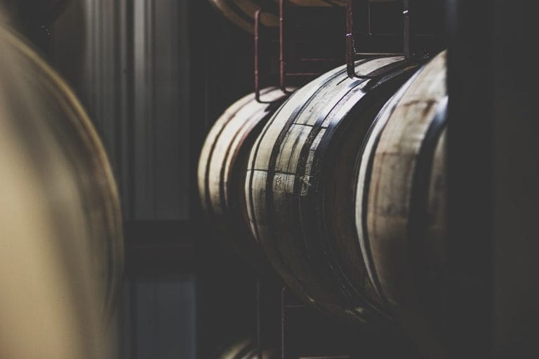 Rows of charred oak bourbon barrels stacked inside a Kentucky distillery warehouse.