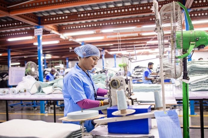 Workers on an industrial appliance assembly line moving large white refrigerator units down a conveyor.
