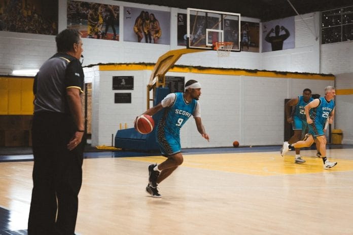 A women's college basketball player driving toward the rim during a conference tournament game, defenders setting up in the lane.