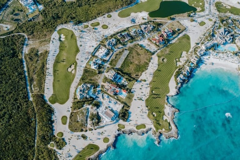 A par-three island green golf hole surrounded by water, with a small bridge leading out to the green and a sand bunker visible at its edge.
