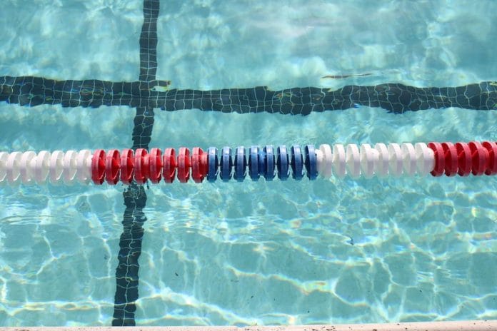An empty competition swimming pool with lane lines stretched across still blue water under overhead lights.