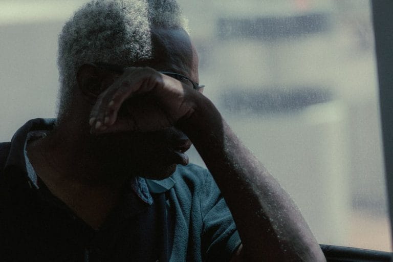 An older man sits close to a television showing a college basketball broadcast, with a notepad on his lap.