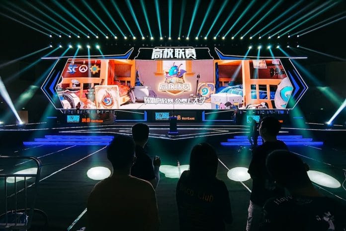 A brightly lit draft stage with a podium and large screens, photographed from the floor of a packed venue.