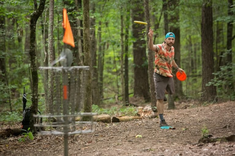 A cornhole bag mid-flight toward a wooden board at an outdoor tournament