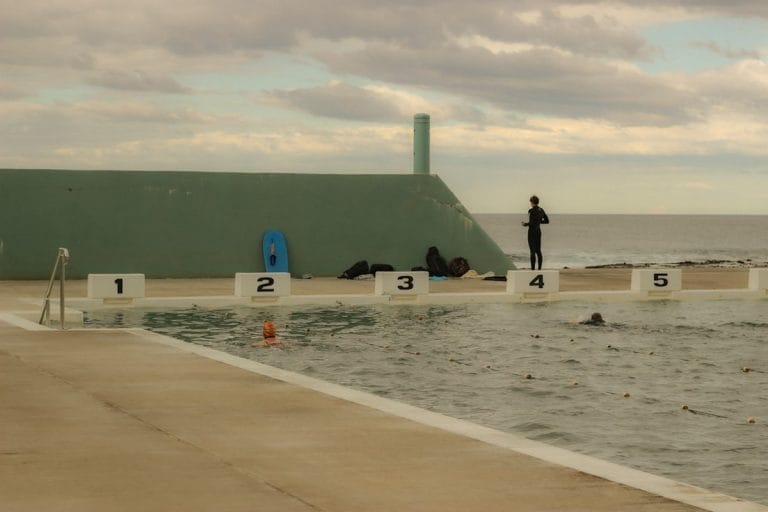 A small-town public swimming pool with empty lanes and a lifeguard chair under bright midday sun