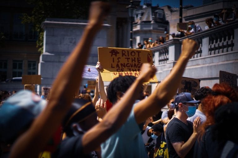 A dense crowd of May Day marchers fills a downtown American street, holding handmade signs about workers' rights.