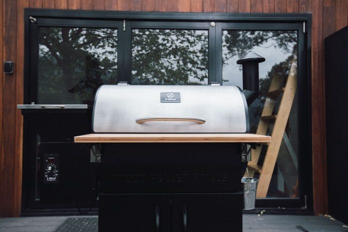 A large smoked brisket resting on a cutting board beside a backyard pellet smoker