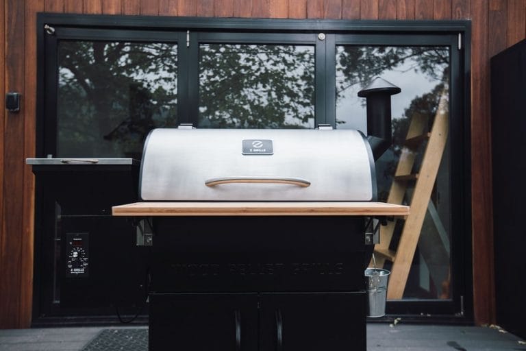 A large smoked brisket resting on a cutting board beside a backyard pellet smoker