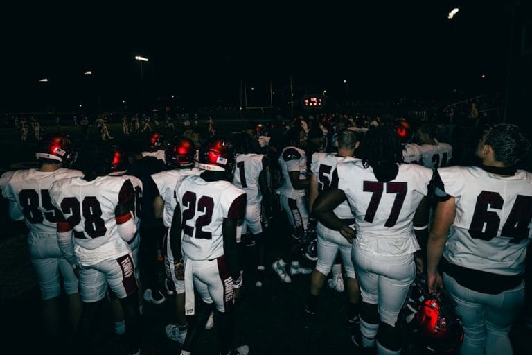 A small-town high school football concession stand at night with nachos, hot dogs, and bright orange cheese sauce under fluorescent lighting.