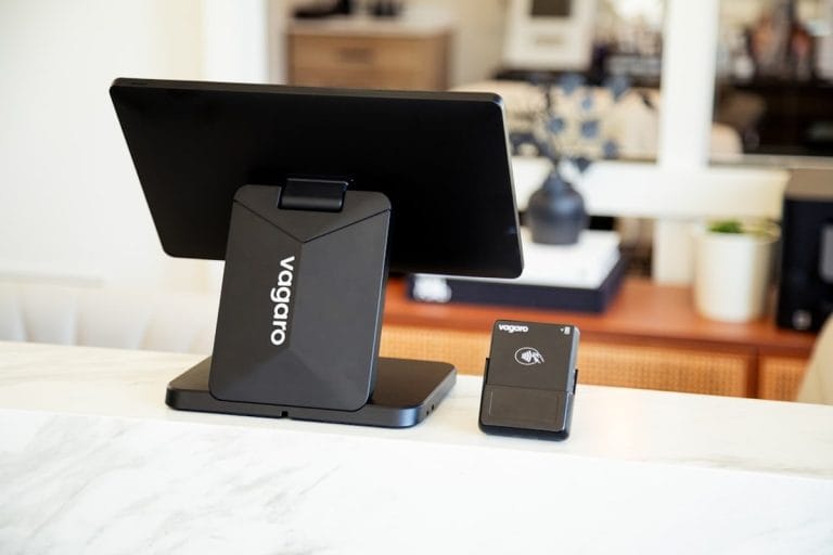 A credit card payment terminal sitting on the wooden counter of a small bakery next to a tray of pastries.
