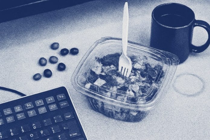FOMC Day Desk An overhead view of a trader's desk during an FOMC announcement: half-eaten salad with a fork stabbed through the lid, scattered candy, coffee mug ring on paper.