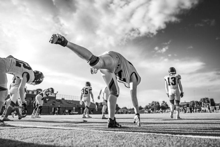 A high school junior varsity football team gathered on a practice field in early fall afternoon light