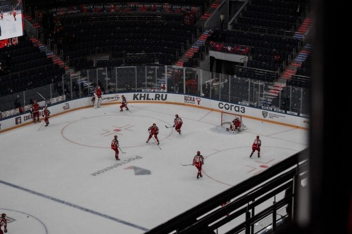 Two women's ice hockey players battle for the puck along the boards during a fast-paced game.