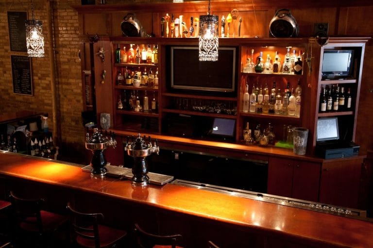 Interior of a small-town tavern with a television mounted above the bar and a few regulars on stools