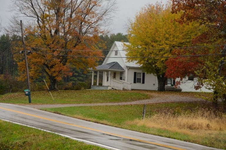 A weathered rural mailbox on a quiet country road in early autumn, leaves beginning to turn.