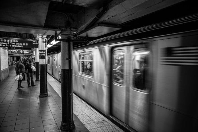 A 7 train platform in Queens, New York, with commuters waiting under fluorescent station lighting.