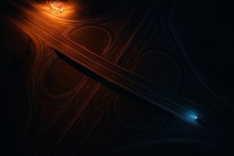Overhead night view of an empty highway interchange split between warm amber and cold blue light.