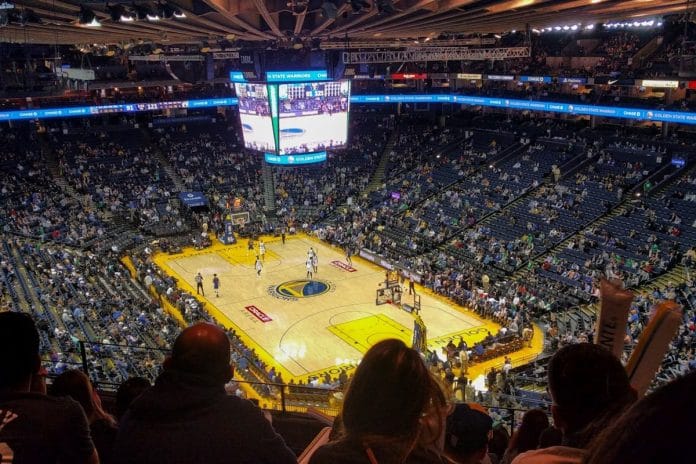 A packed NBA arena lit in red and green during a Christmas Day game, with a basketball mid-air over the court.