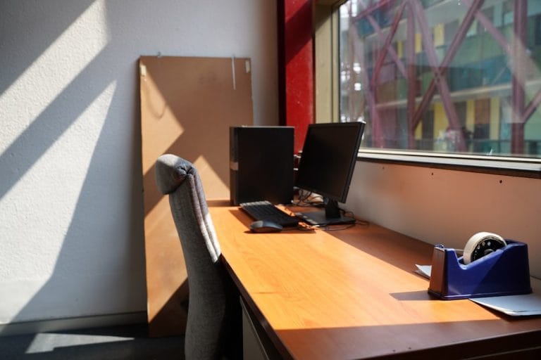 A beige office cubicle with a desktop monitor, paperwork, and a small framed photo on the desk.